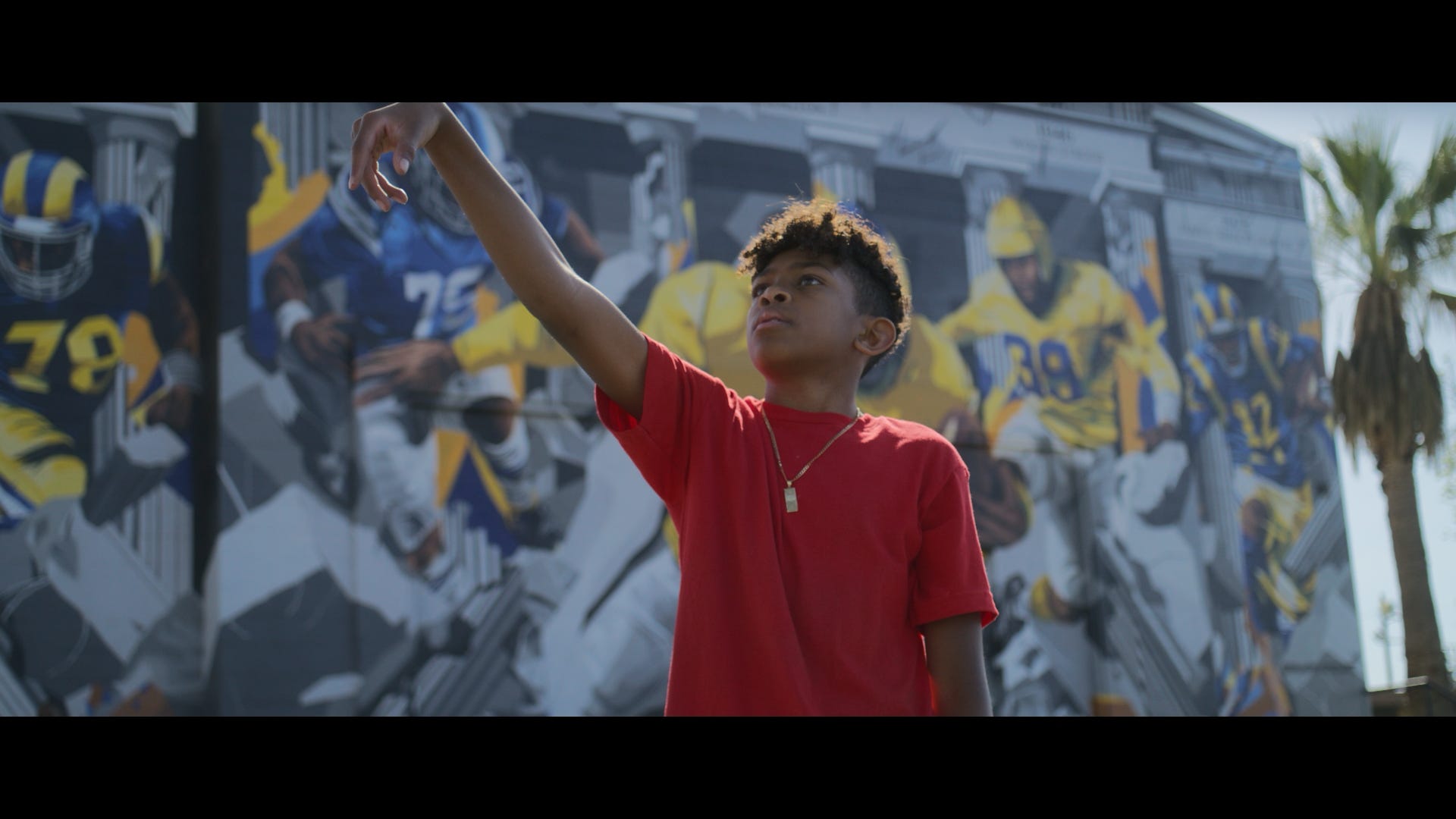Film still — boy reaching toward mural