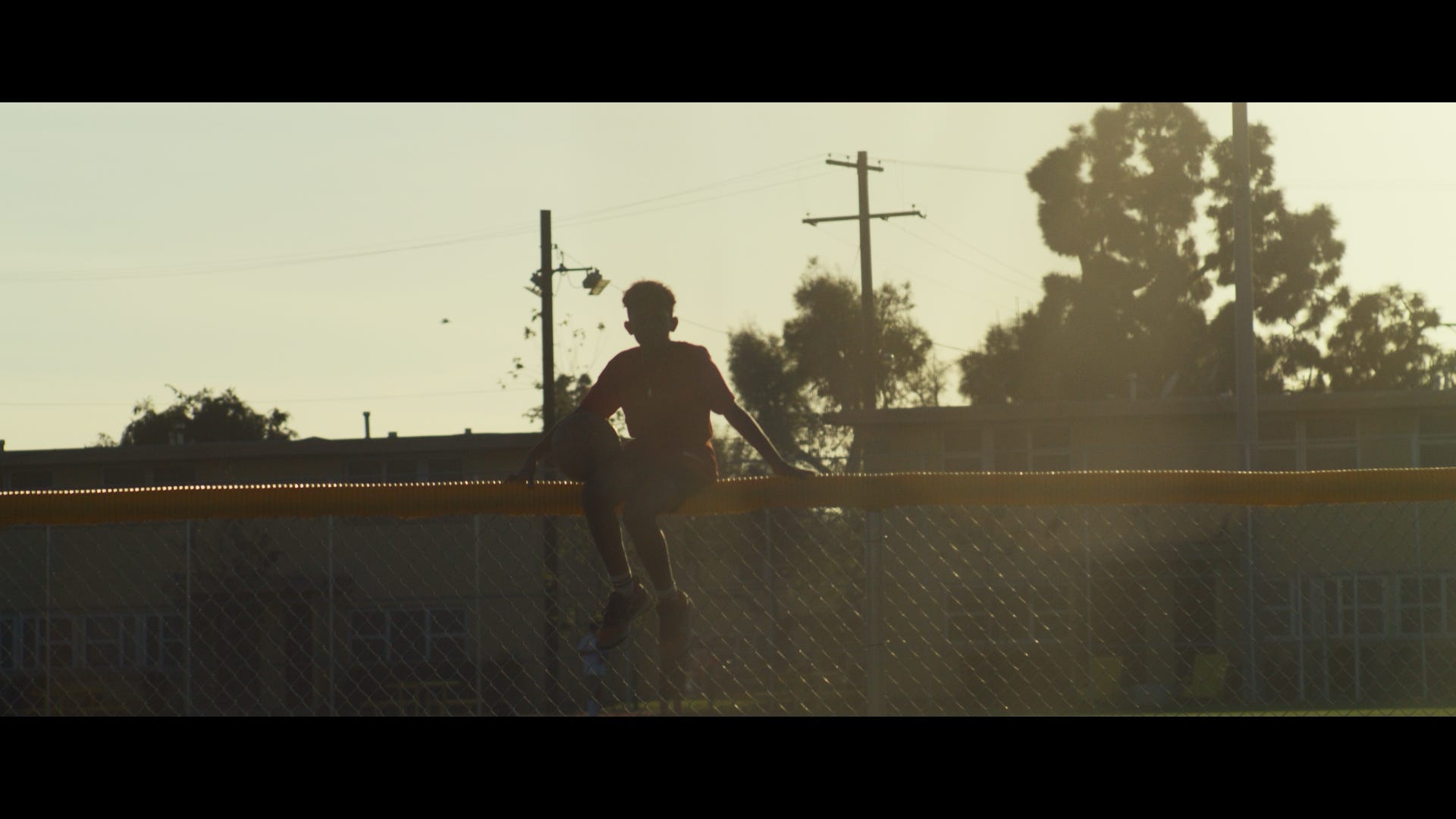 Film still — silhouette against fence at sunset
